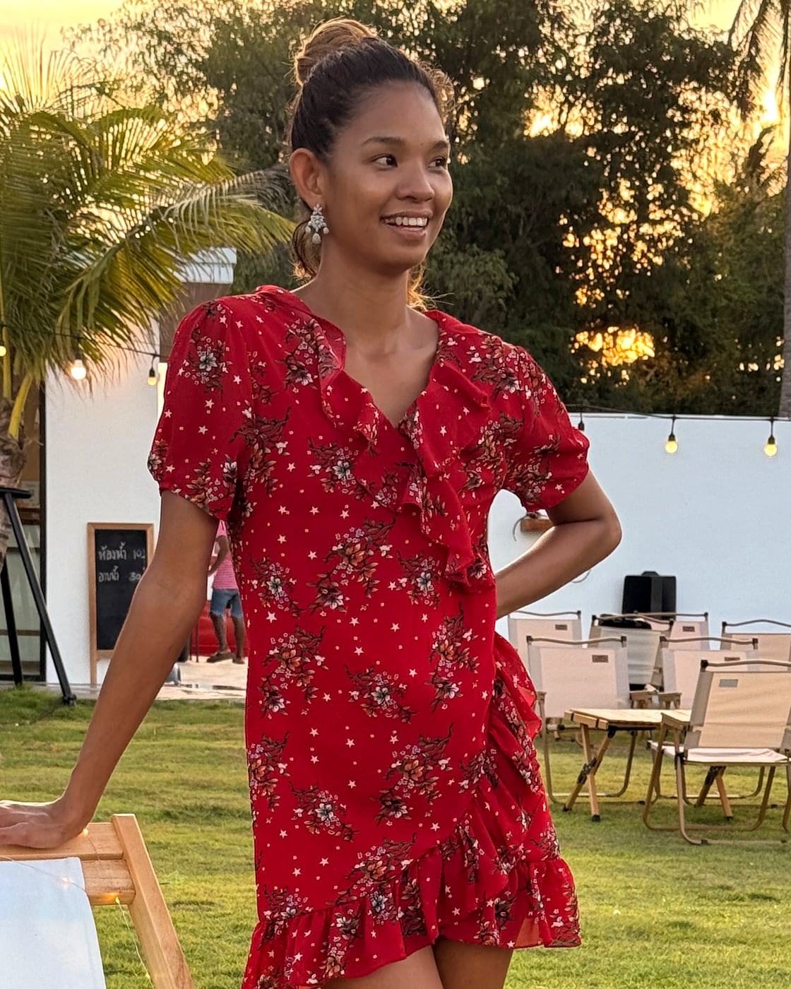 Alise Pomanee, the firm's principal, smiling in warm golden-hour light in a red floral dress at a garden by the coast.
