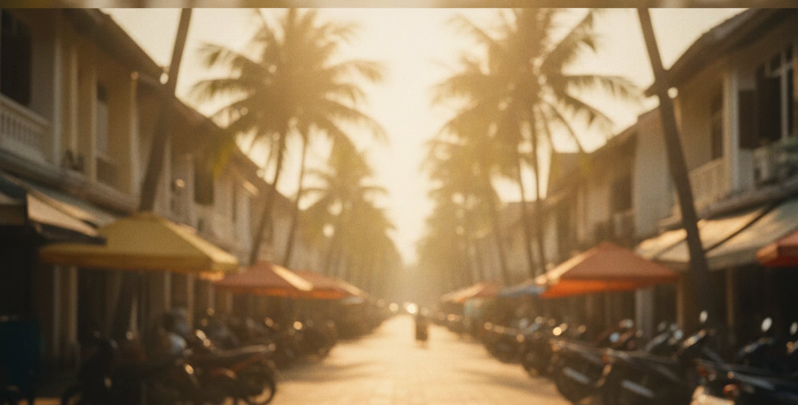 A warm golden-hour street in a tropical Southeast Asian city: low sun between palm trees and shophouses, an anonymous everyday street.
